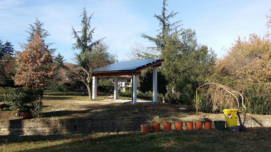 Capanno con tettoia in giardino, alberi e vasi.